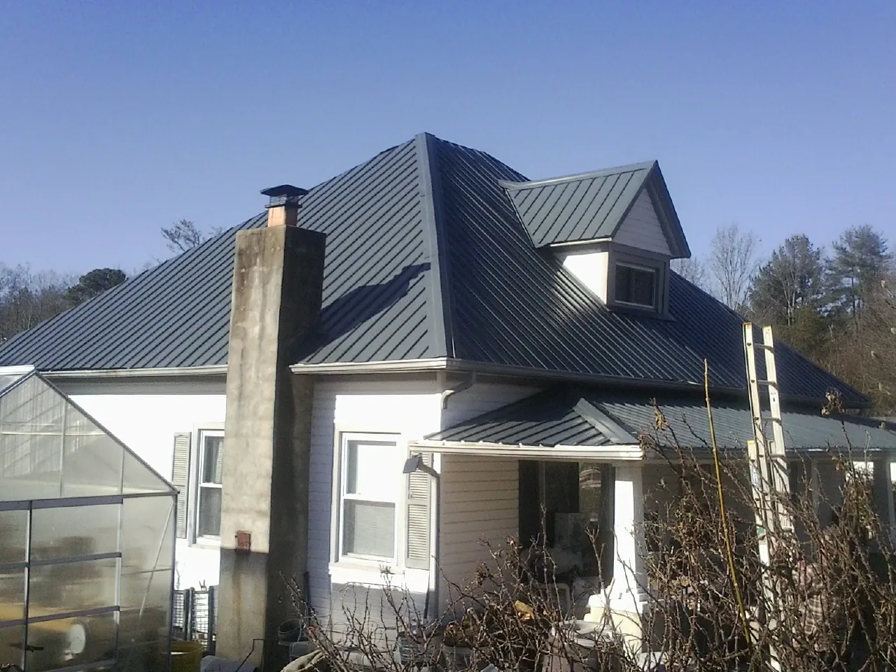 Dark blue standing seam metal roof on a white farmhouse with dormer — Slate & Tile Roof Repair by Roofing Brothers in Sunburg