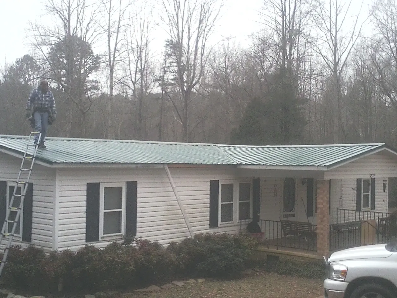 Worker on a ladder beside a new green metal roof on a ranch home in Sunburg