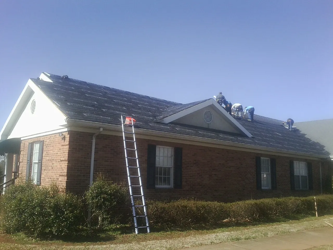 Crew tearing shingles off a brick ranch roof with a ladder set — Metal Roof Repair work by our crew in Sunburg