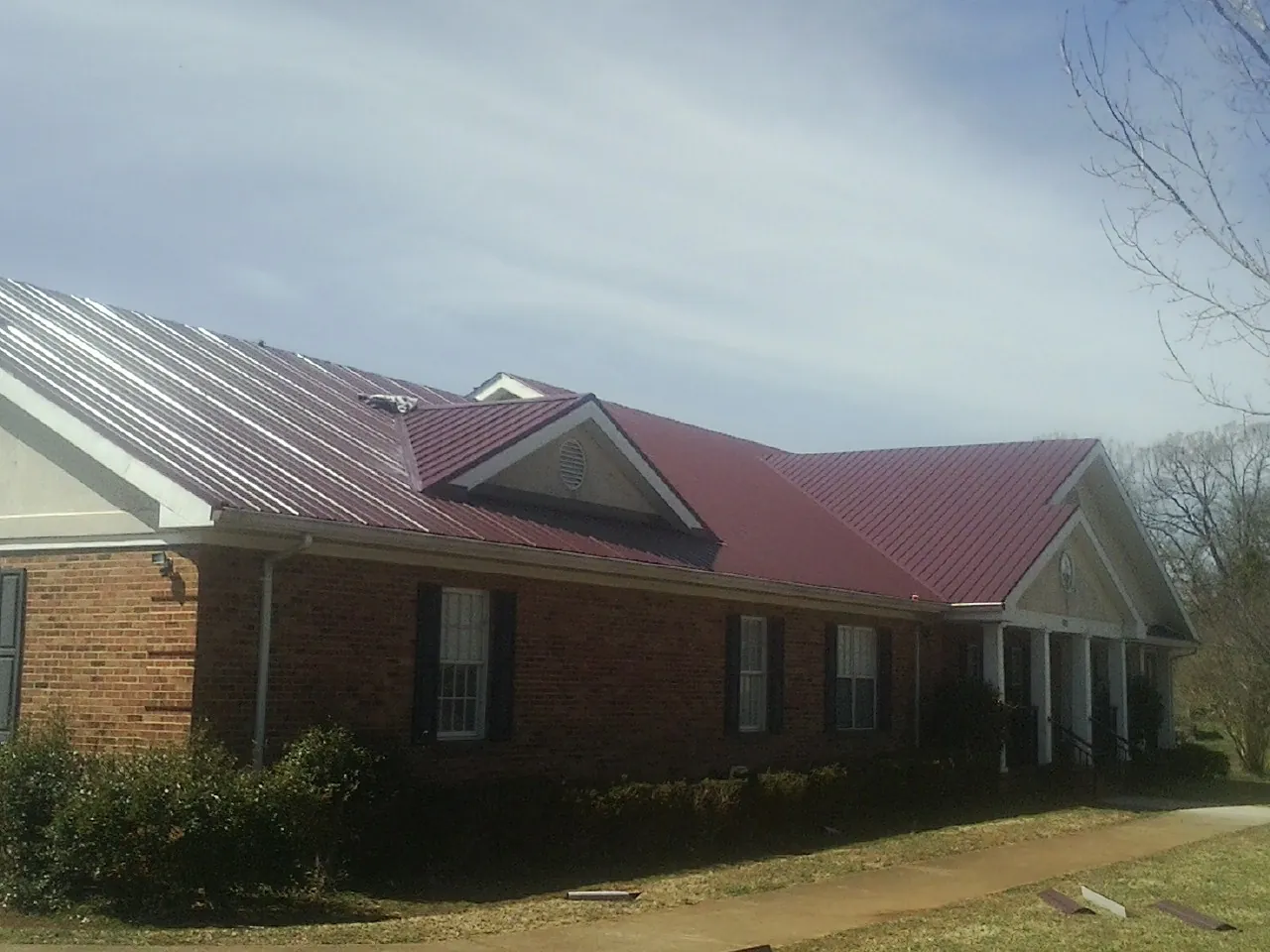 Red metal roof with gabled entries on a long brick building, from a Hail Damage Roof Repair job in Sunburg