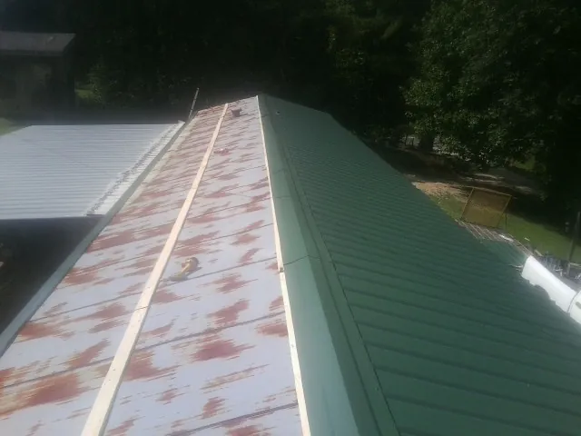 Old rusted panels beside newly installed green metal roofing — Wind Damage Roof Repair by Roofing Brothers in Sunburg