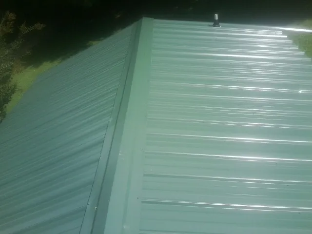 New green metal panels meeting at the ridge of a roof — Flat Roof Repair work by our crew in Sunburg