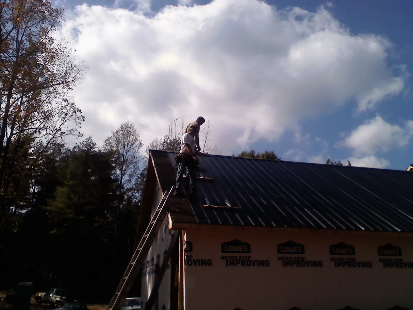 Roofer fastening dark metal panels high against a cloudy sky, from a Roof Inspection job in Sunburg