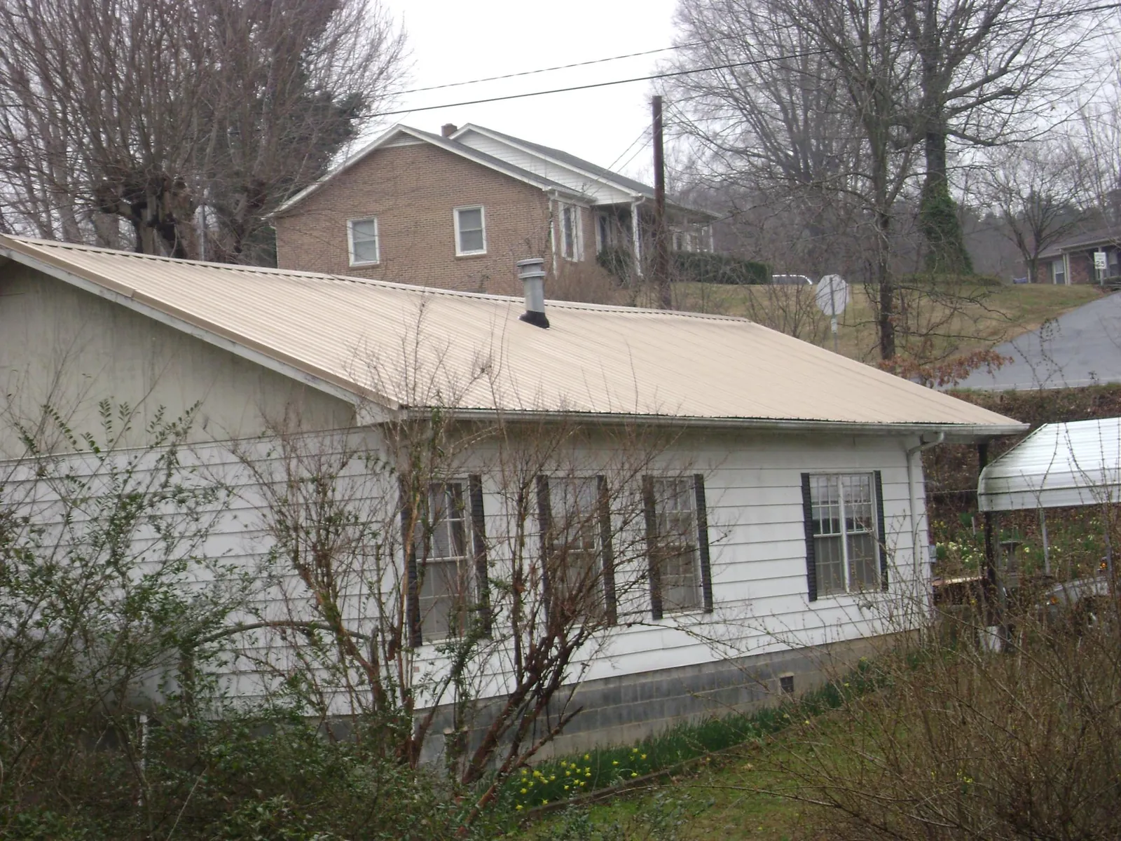 Tan metal roof on a white sided house set into a hillside — Commercial Roofing by Roofing Brothers in Sunburg